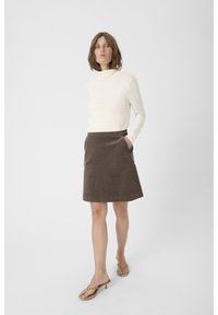 Crème turtleneck met lange mouwen, gecombineerd met een bruine corduroy rok met zakken en een A-lijn silhouet, gedragen met tan kleurige hakken.