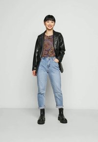 Blazer de pele preta sobre uma blusa com padrão, jeans de cintura alta azul clara e botas de tornozelo pretas. Texturas suaves e ajuste descontraído.