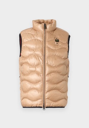 Bež brezrokavnik z oblazinjenjem, visokim ovratnikom, zadrgo spredaj, črnimi notranjimi robovi ter majhno pravokotno črno-rumeno logotipno nalepko na prsih.