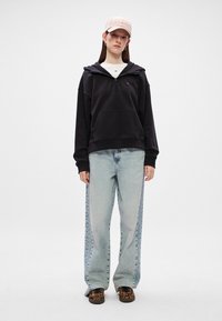 Μαύρο φούτερ με φερμουάρ και μπροστινή τσέπη, ανοιχτό μπλε φαρδύ τζιν με πλευρικές λεπτομέρειες και μαύρα παπούτσια με λεοπάρ σχέδιο. Το ροζ καπέλο ολοκληρώνει την εμφάνιση.