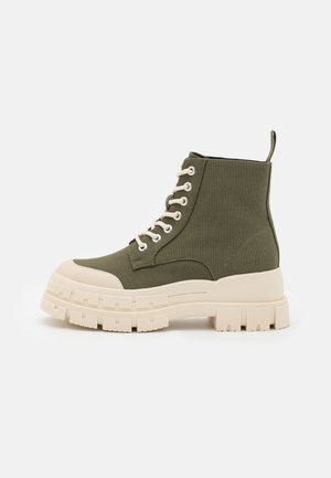Green canvas ankle boots with a chunky white sole, lace-up front, and padded collar. Features a loop tab for easy wear.