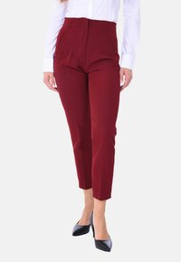 Pantaloni bordeaux a vita alta con frontale plissettato, slim fit e tasche laterali, abbinati a una camicia bianca con bottoni e tacchi neri.