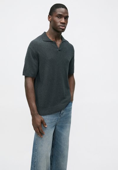 Σκούρο γκρι κοντομάνικο πόλο μπλουζάκι με υφή υφάσματος, που διαθέτει γιακά και άνετη γραμμή, σε συνδυασμό με ανοιχτό μπλε τζιν παντελόνι με ίσια γραμμή.