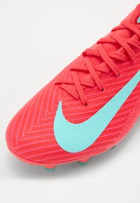 Nike soccer cleat in bright pink with a textured surface, featuring a large aqua swoosh design and green studs on the sole.