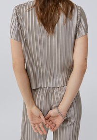Top de satén con rayas verticales en tonos beige y plateados, con mangas cortas y un corte holgado, combinado con pantalones a rayas a juego y una pulsera plateada.