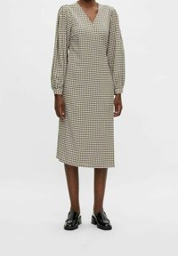 Ruudullinen midi-mekko kermanvärisenä ja mustana, jossa on V-pääntie, pallosilateet ja suora siluetti. Yhdistetty kiiltäviin mustiin loafereihin.
