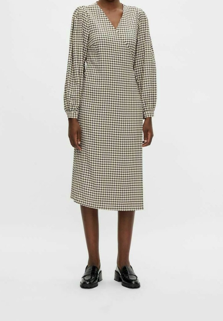 Ruudullinen midi-mekko kermanvärisenä ja mustana, jossa on V-pääntie, pallosilateet ja suora siluetti. Yhdistetty kiiltäviin mustiin loafereihin.