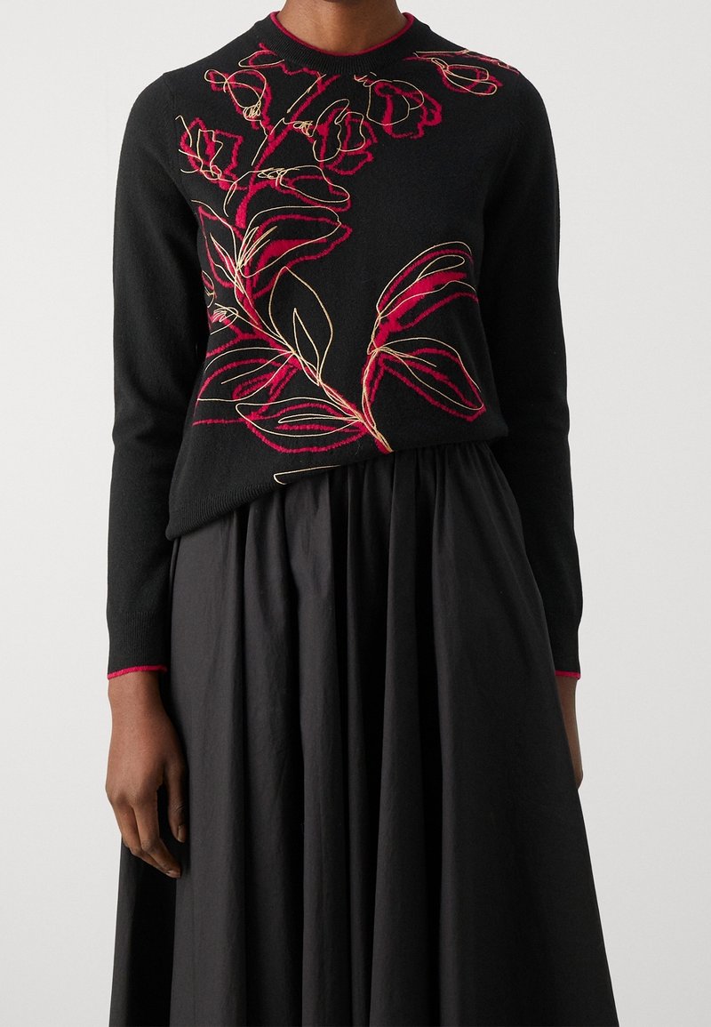Black sweater with red and gold floral embroidery, round neck, and long sleeves. Worn over a textured black skirt.