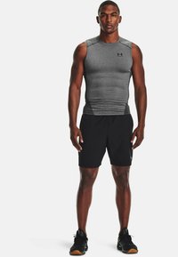 Gray athletic sleeveless shirt paired with black shorts. Features a fitted design with smooth fabric and logo accents. Footwear is black with patterned soles.