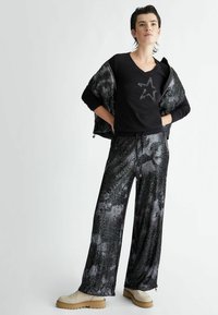 Top nero a V con grafica a stella, abbinato a pantaloni larghi scintillanti in tonalità di nero e grigio, completato da una giacca zippata testurizzata.