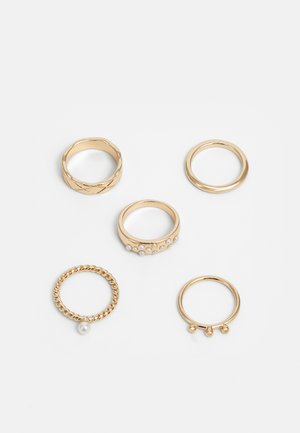 Five gold rings with varying designs: one braided, one with pearls, smooth polished, and a beaded detail. Different widths and textures.