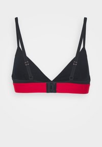 Svart bomulls-bralette med röd elastisk rem, vik-design, justerbara band och en krok-och-ögla-stängning på baksidan.