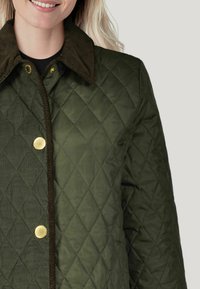 Olivgrüne gesteppte Jacke mit Cordkragen und goldenen Druckknöpfen. Verfügt über ein Rautenmuster und eine glatte Textur.