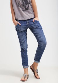 Dżinsy w średnim niebieskim kolorze, o luźnym kroju, z podwiniętymi mankietami i dwiema przednimi kieszeniami. Zestawione z szarym t-shirtem z grafiką i sandałami.