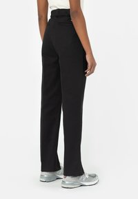 Pantalones rectos negros con una cintura alta, que cuentan con bolsillos traseros y un tejido suave. Combinados con zapatillas deportivas grises.