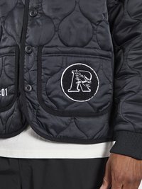 Chaqueta de abrigo negra con acolchado, cierre de botones, puños acanalados y dos grandes bolsillos parche con un logo bordado en uno de ellos.