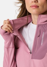 Veste à zip rose avec une doublure intérieure texturée, dotée d'un extérieur lisse, d'une poche latérale et d'un accent logo sur la poitrine.