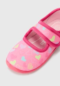 Rozā bērnu apavi ar sirdīšu rakstiem, kuriem ir gluda tekstūra, divi Velcro jostas un noapaļota pirksta forma.