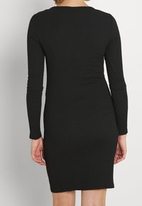 Vestito nero aderente con maniche lunghe, tessuto texture e design applicato. Presenta un collo tondo e una lunghezza sopra il ginocchio.