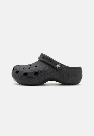 Black slip-on clog with ventilation holes and adjustable heel strap, textured surface, and rubber sole on plain background.