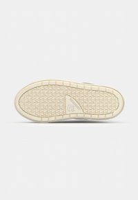 Semelle de chaussure avec une bande de roulement en caoutchouc beige présentant un motif triangulaire et le logo Converse près de la zone de la voûte plantaire.