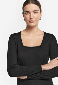 Svart långärmad topp med fyrkantig halsringning, ribbat mönster och figurnära design. Med diskreta sömnadsdetaljer längs kanterna.