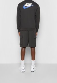 Tmavě šedá mikina Nike s modrým logem na zádech, doplněná o odpovídající cargo kraťasy a bílé tenisky s námořnickými akcenty.