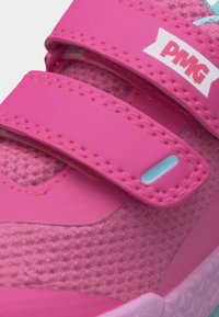 Κοντινό πλάνο ενός ροζ παιδικού αθλητικού παπουτσιού με υφασμάτινη υφή και δύο ρυθμιζόμενα λουριά με βέλκρο, το ένα με ετικέτα "PMG".