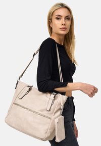 Beige neplederen handtas met twee handvatten, een ritssluiting aan de voorkant, een verwijderbaar klein tasje en contrasterende hardwareaccenten.