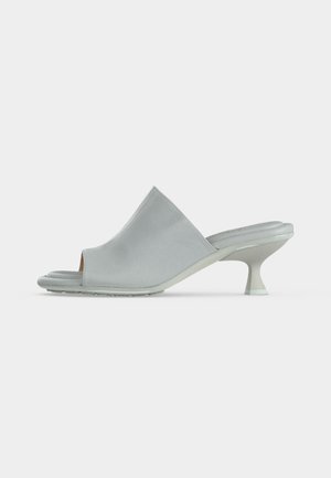 Weißer offener Peeptoe-Mule mit gepolsterter Sohle und einem geschwungenen, mittelhohen Kittenabsatz vor einfarbigem Hintergrund.