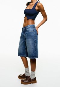 Denim bermudashorts i medium blått med rak skärning och fåll. Matchat med en marinblå ribbad crop top och bruna texturerade snörskor.