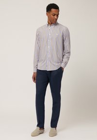 Gestreepte overhemden in lichtblauw, geel en wit, met een spread collar en lange mouwen. G gedragen met marineblauwe broek en lichte schoenen.