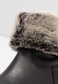 Černé kožené kotníkové boty s měkkým šedým umělým kožíškem na lemu. Obsahují švy a mají zaoblený tvar. Hladký povrch s teplým vzhledem.