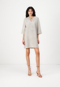 Vestido em padrão xadrez creme e preto com decote em forma de olho de fechadura, mangas três-quartos e um corte descontraído. Combinado com sandálias de salto alto bege com tiras.