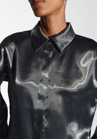 Glanzend zwart shirt met een gladde textuur, knoopsluiting aan de voorkant en een klassieke kraag. De stof heeft een subtiele metallic glans.