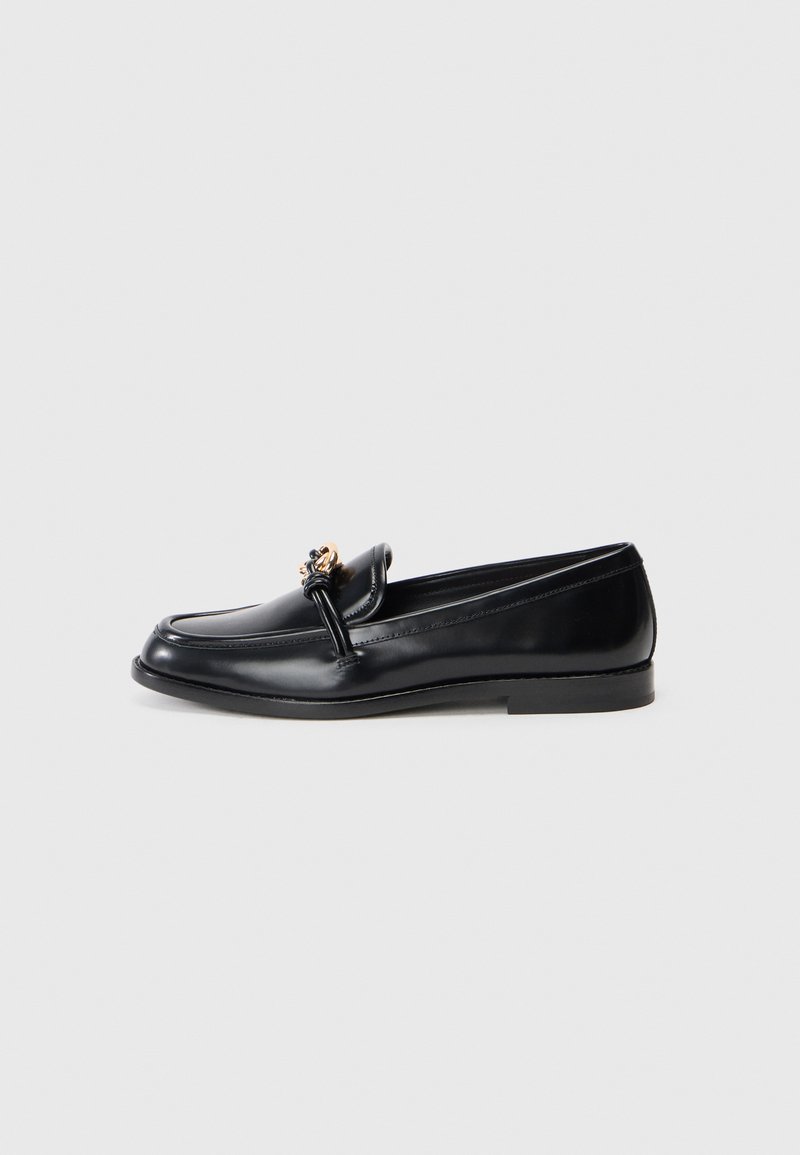 Black leather loafer with a smooth finish, featuring a decorative gold-tone hardware accent on the front. Low-profile design and rounded toe.