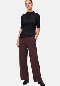 Zwarte textuur top met een hoge hals en korte mouwen, gecombineerd met brede bordeauxrode broek en zwarte schoenen.