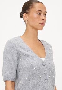 Grijze gebreide cardigan met korte mouwen, voorzien van parel- en rhinestoneversieringen, een V-hals en ronde knopen aan de voorkant.