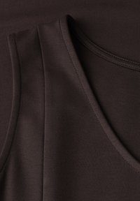 Gros plan d'un vêtement sans manches marron foncé avec des coutures visibles et un tissu lisse légèrement texturé.
