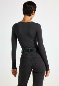 Maglietta a maniche lunghe, aderente, di colore grigio scuro con scollatura tonda, abbinata a jeans neri a vita alta con una cintura nera e tasche.