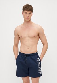 Marineblaue Badeshorts mit elastischem Bund und Kordelzug. Mit einem weißen vertikalen Logo auf der linken Seite. Leichter, glatter Stoff.