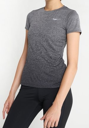 Femme portant un t-shirt de sport Nike gris dégradé à manches courtes et un legging noir, debout, les bras détendus le long du corps.