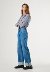 Striped button-up shirt with long sleeves, paired with high-waisted, wide-leg blue jeans with rolled cuffs and black loafers.