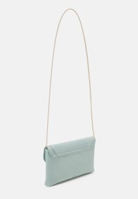 Bolso de mano de ante verde menta con una larga correa de cadena dorada y cierre de solapa. Textura suave, diseño minimalista.