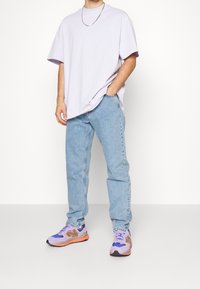 T-shirt ample violet clair, jean en denim bleu et baskets multicolores avec accents en maille et semelles en caoutchouc. Tenue décontractée.