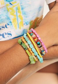 Bunte Perlenarmbänder in verschiedenen Formen, mit türkisfarbenen, pinken, gelben, grünen und orangefarbenen Perlen mit glatten und strukturierten Oberflächen.