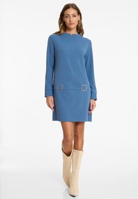 Blaues Shiftkleid mit langen Ärmeln, einem ausgeschnittenen Ausschnitt und goldenen quadratischen Akzentdetails in der Taille. Glattes Material und knielanger Schnitt.