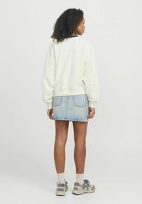 Felpa crema con spalle scese, abbinata a una gonna di jeans azzurro chiaro. Presenta polsini elasticizzati e orlo dritto. Sneakers grigie completano l'outfit.