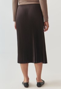 Jupe midi plissée noire, fabriquée dans un tissu léger. Présente une texture lisse avec des plis profonds et réguliers, et une taille ajustée.