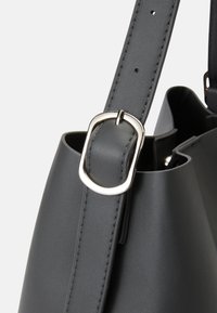 Sac à main en cuir gris avec une texture lisse, comportant une boucle en métal argenté et une sangle, ainsi qu'un design effilé.